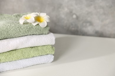 Photo of Fresh terry towels and plumeria flowers on white table, closeup. Space for text