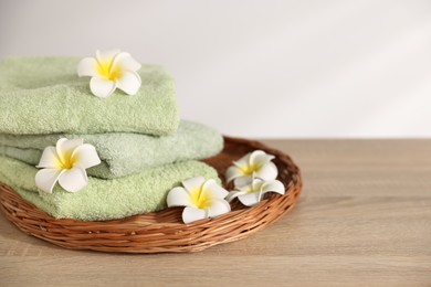 Photo of Fresh terry towels and plumeria flowers on wooden table. Space for text