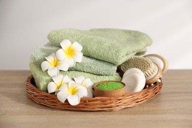 Photo of Fresh terry towels, cosmetic products, brush and plumeria flowers on wooden table