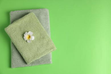 Photo of Fresh terry towels and plumeria flower on green background, top view. Space for text