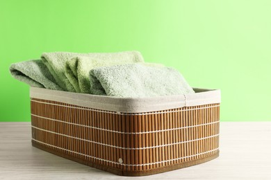 Photo of Fresh terry towels in basket on white table