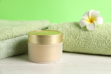 Photo of Fresh terry towels, cosmetic product and plumeria flower on white wooden table, closeup