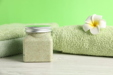 Photo of Fresh terry towels, cosmetic product and plumeria flower on white wooden table, closeup