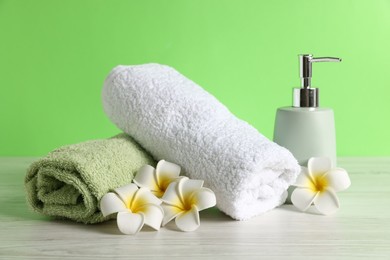 Photo of Fresh terry towels, soap dispenser and plumeria flowers on white wooden table