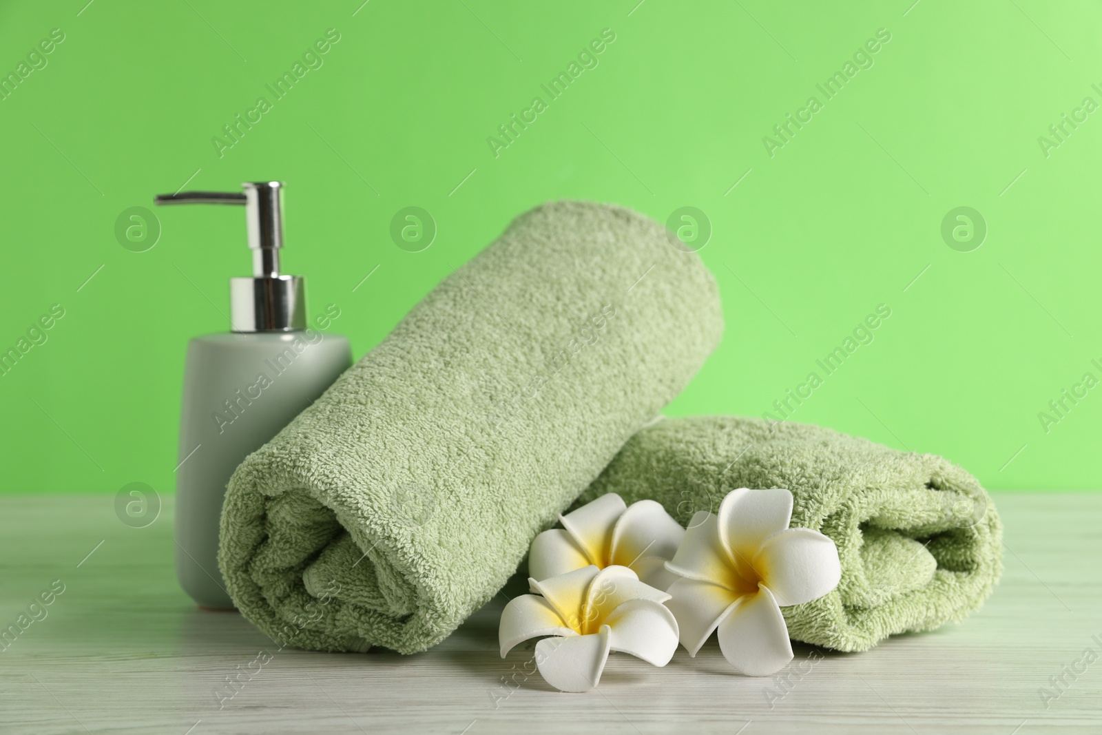 Fresh terry towels, soap dispenser and plumeria flowers on white wooden table Photo of Fresh terry towels, soap dispenser and plumeria flowers on white wooden table