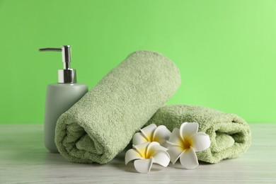 Photo of Fresh terry towels, soap dispenser and plumeria flowers on white wooden table