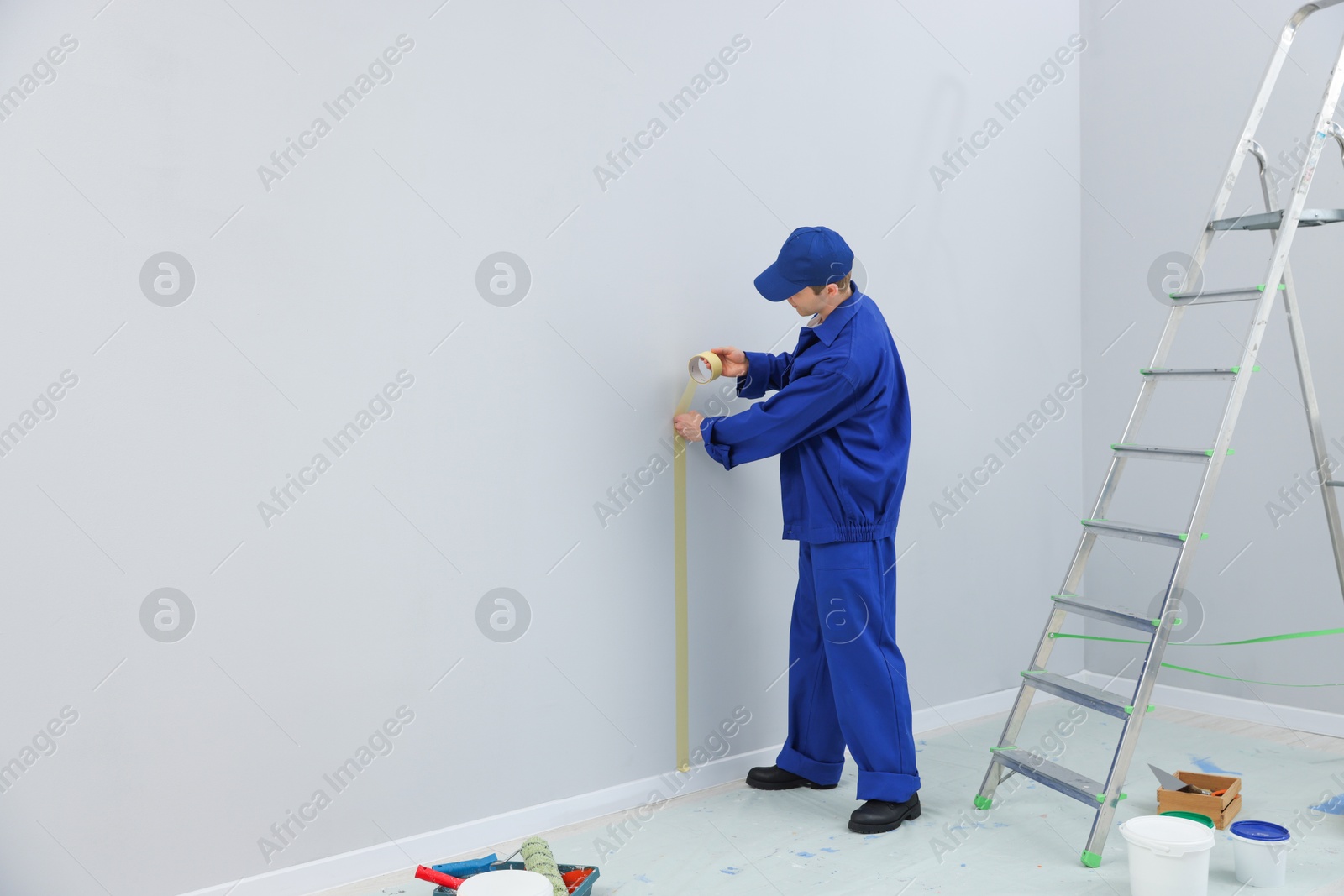Worker putting painter's tape on wall in room. Space for text Photo of Worker putting painter's tape on wall in room. Space for text