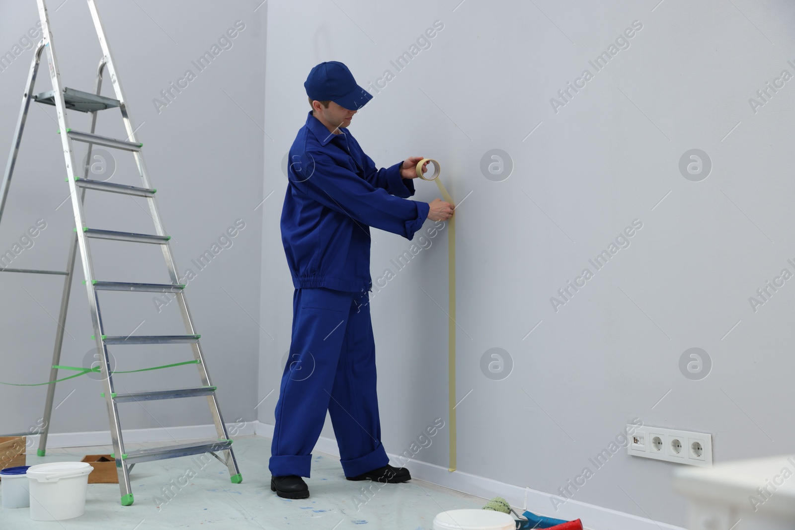 Worker putting painter's tape on wall in room. Space for text Photo of Worker putting painter's tape on wall in room. Space for text