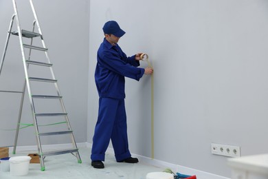 Photo of Worker putting painter's tape on wall in room. Space for text