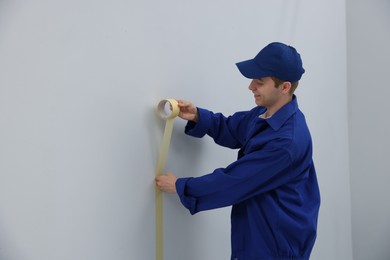 Photo of Worker putting painter's tape on wall in room. Space for text