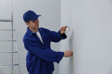 Photo of Worker putting painter's tape on wall in room