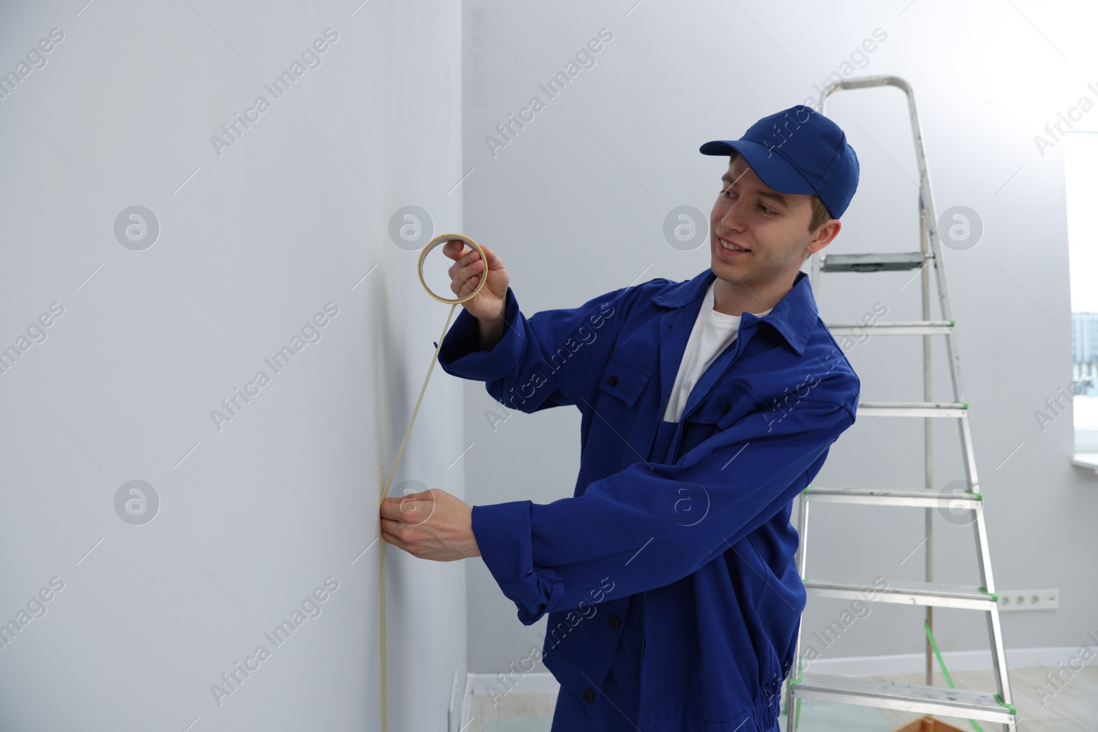 Photo of Worker putting painter's tape on wall in room