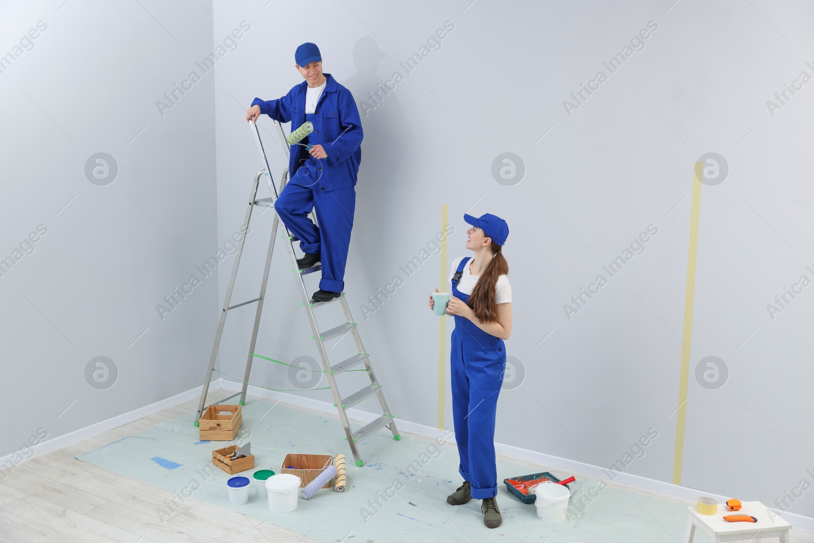 Woman with coffee and man on ladder renovating room Photo of Woman with coffee and man on ladder renovating room