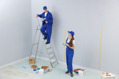 Photo of Woman with coffee and man on ladder renovating room