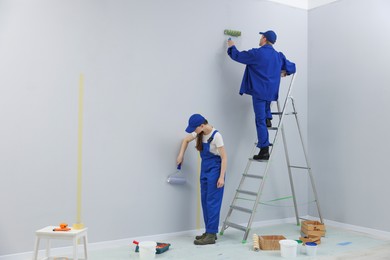 Photo of Workers painting wall with rollers in room