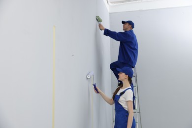 Photo of Workers painting wall with rollers in room
