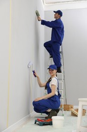 Photo of Workers painting wall with rollers in room
