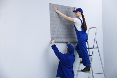 Photo of Workers putting wallpaper on wall in room. Space for text