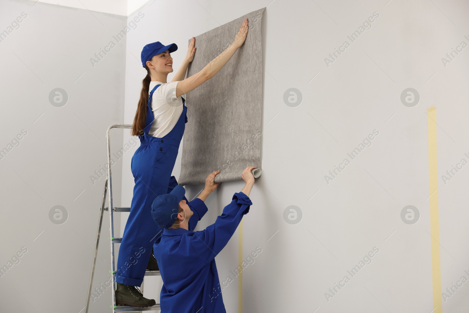 Workers putting wallpaper on wall in room. Space for text Photo of Workers putting wallpaper on wall in room. Space for text