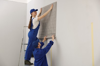 Photo of Workers putting wallpaper on wall in room. Space for text