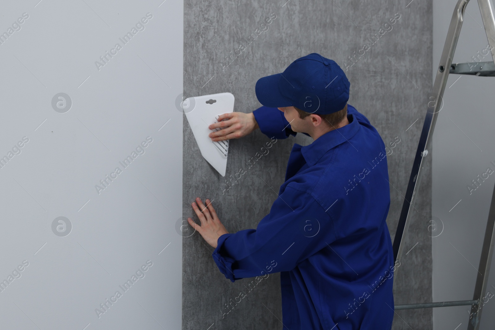 Worker smoothing wallpaper with tool in room Photo of Worker smoothing wallpaper with tool in room