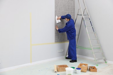 Photo of Worker smoothing wallpaper with tool in room. Space for text