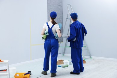 Photo of Workers with rolls of wallpapers in room, back view