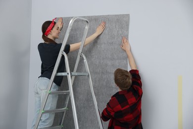 Photo of Happy couple putting wallpaper on wall in room