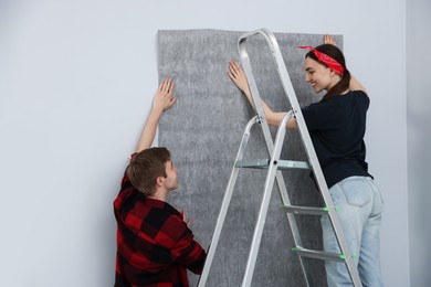 Photo of Happy couple putting wallpaper on wall in room