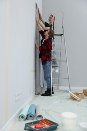 Photo of Happy couple putting wallpaper on wall in room