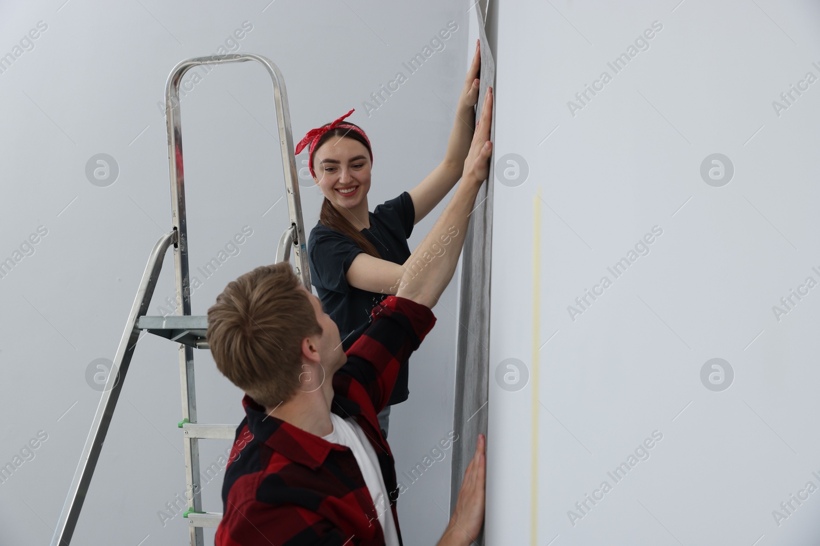 Happy couple putting wallpaper on wall in room Photo of Happy couple putting wallpaper on wall in room