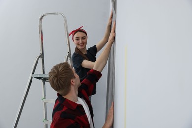 Photo of Happy couple putting wallpaper on wall in room