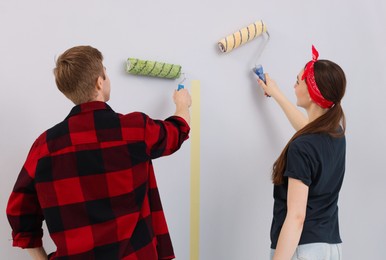 Photo of Couple painting wall with rollers in room, back view