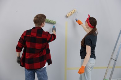 Photo of Couple painting wall with rollers in room, back view