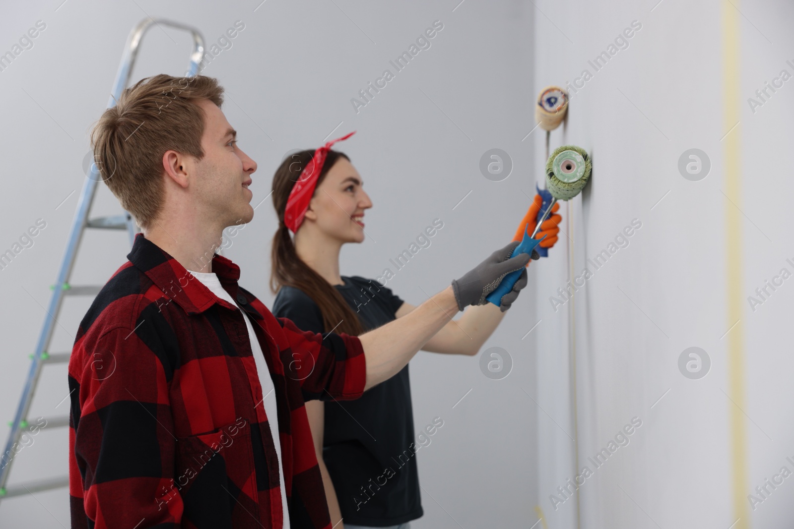 Couple painting wall with rollers in room Photo of Couple painting wall with rollers in room