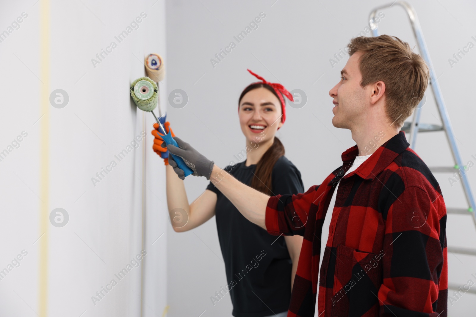 Couple painting wall with rollers in room Photo of Couple painting wall with rollers in room