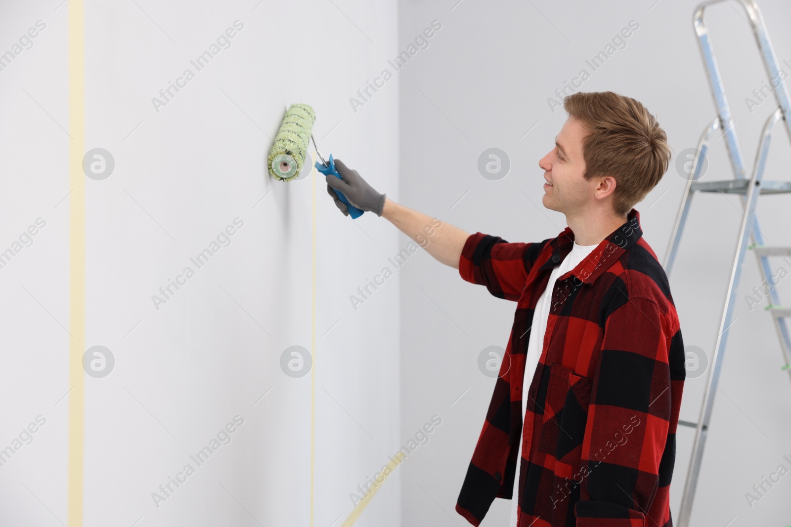 Man painting wall with roller in room Photo of Man painting wall with roller in room