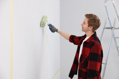 Photo of Man painting wall with roller in room