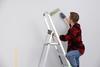 Photo of Man on ladder painting wall with roller in room. Space for text