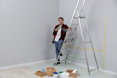 Photo of Man with roller and ladder in room. Space for text