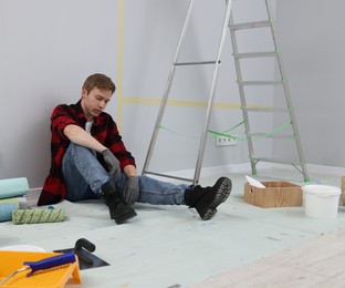 Photo of Tired man having break during renovation in room
