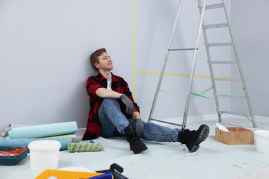 Photo of Tired man having break during renovation in room