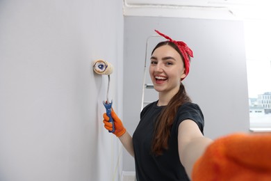 Photo of Happy woman taking selfie while painting wall with roller in room