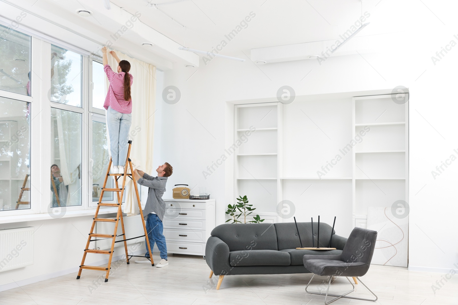 Couple putting up curtains using ladder in room Photo of Couple putting up curtains using ladder in room
