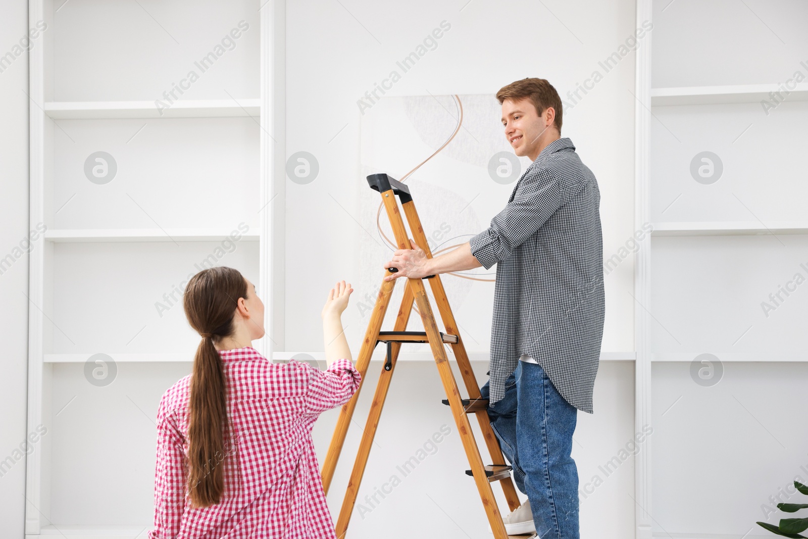 Couple putting painting on wall using ladder at home Photo of Couple putting painting on wall using ladder at home