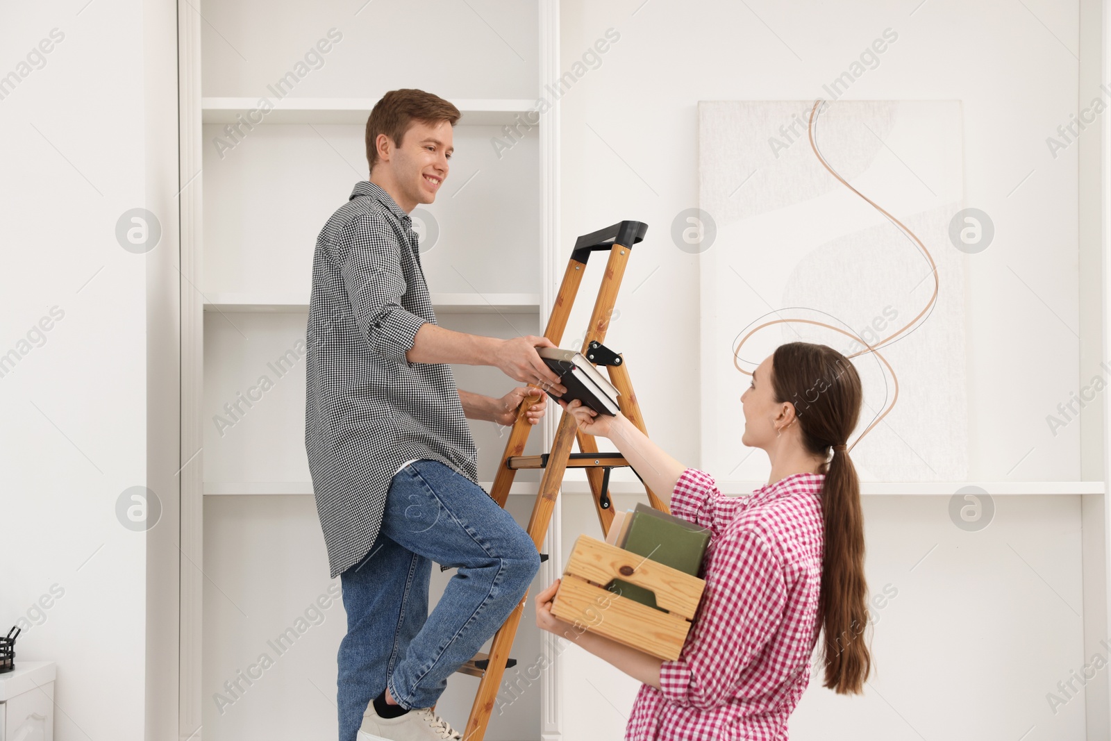 Couple putting books on shelves using ladder at home Photo of Couple putting books on shelves using ladder at home