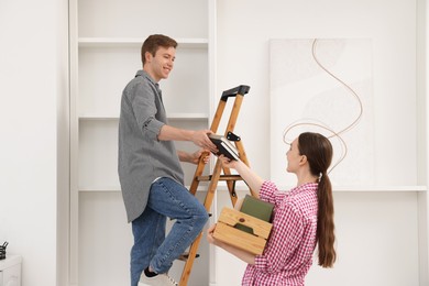 Photo of Couple putting books on shelves using ladder at home