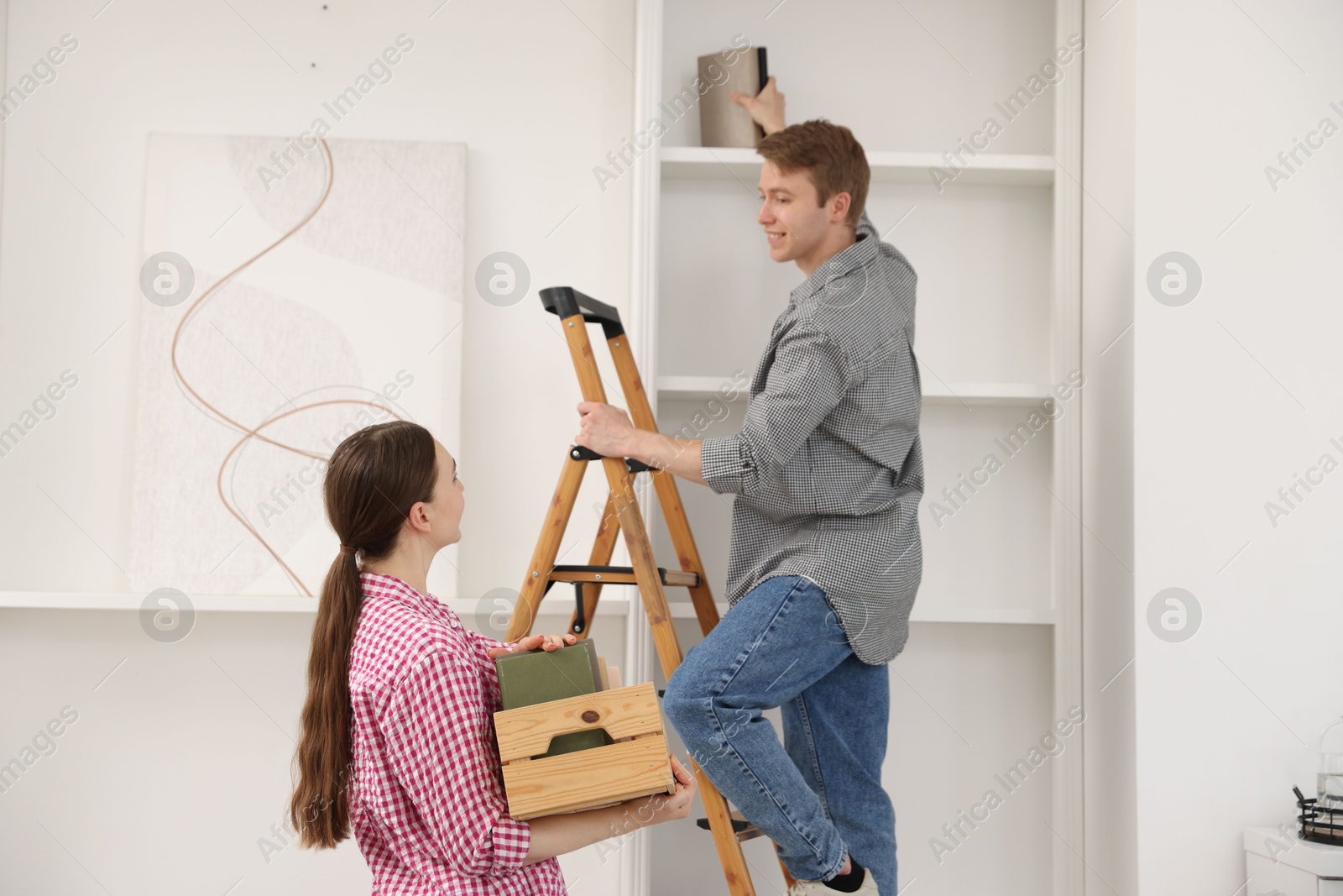 Couple putting books on shelves using ladder at home Photo of Couple putting books on shelves using ladder at home