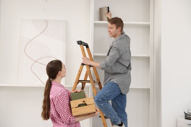 Photo of Couple putting books on shelves using ladder at home