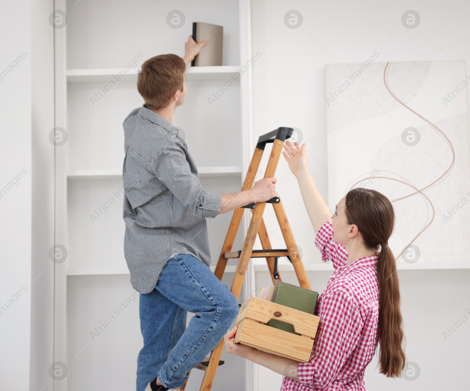 Couple putting books on shelves using ladder at home Photo of Couple putting books on shelves using ladder at home